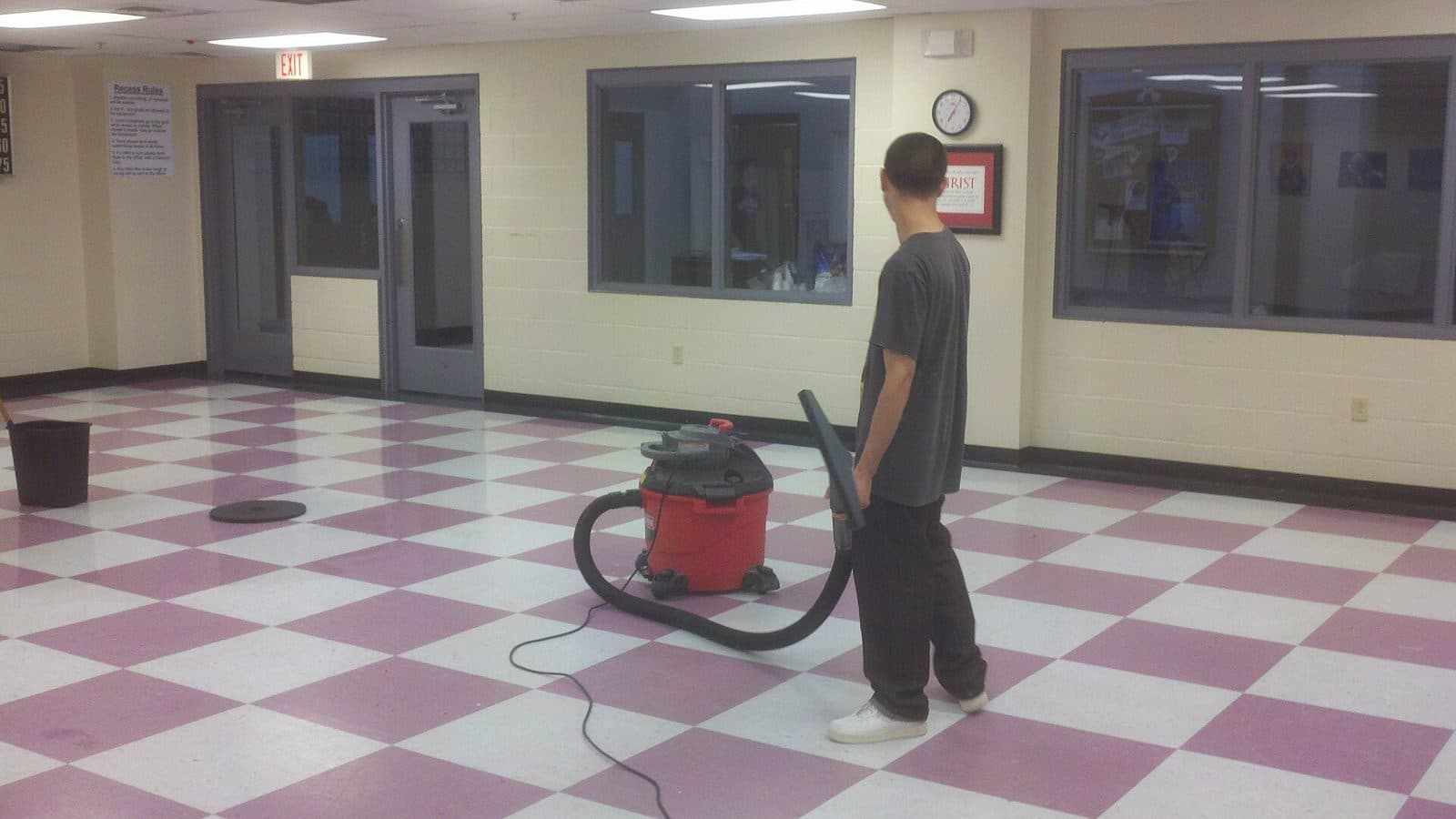 A cleaner vacuuming a corridor in an office building, the kind of work covered by a government cleaning contract